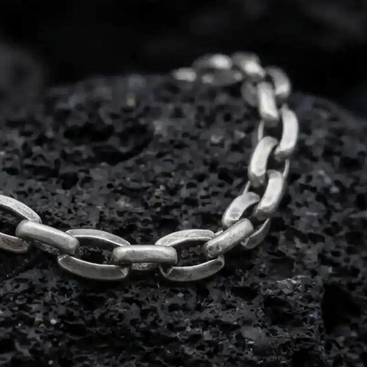 Oxidized sterling silver anchor link bracelet arranged on black volcanic rock, showing its rounded mariner-style links.