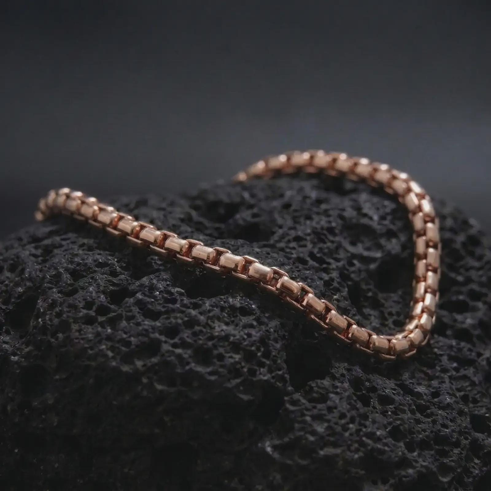 Rose gold plated square link bracelet displayed on lava stone, combining warm tone with a structured low-profile chain design.