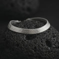 Load image into Gallery viewer, Polished silver herringbone chain bracelet arranged on dark volcanic stone with a clean reflective surface and precise link pattern.
