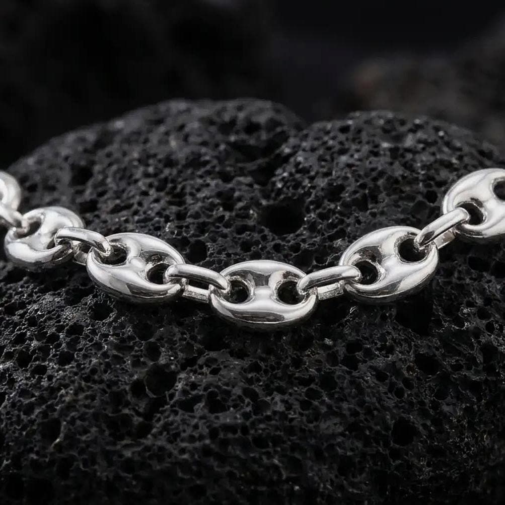 The polished silver 11mm mariner necklace is arranged across textured black volcanic rock, highlighting its broad nautical links, smooth contours, and articulated construction in a premium macro photograph.