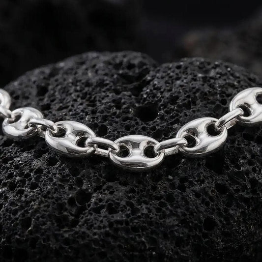 The polished silver 11mm mariner necklace is arranged across textured black volcanic rock, highlighting its broad nautical links, smooth contours, and articulated construction in a premium macro photograph.