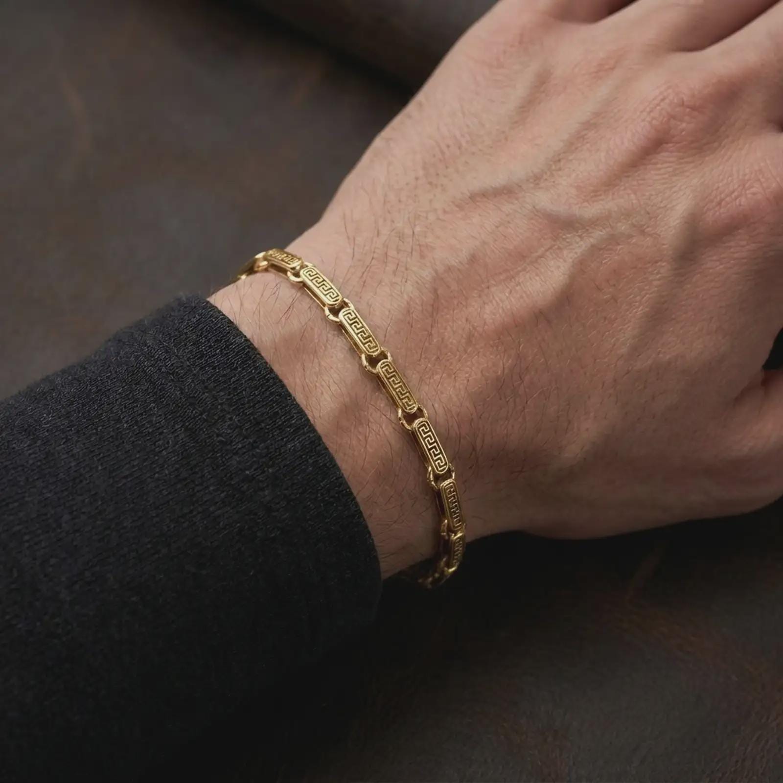 Gold plated Greek key chain bracelet worn on a man’s wrist in an elegant close-up lifestyle photograph.
