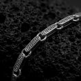 Load image into Gallery viewer, Greek key bracelet with an oxidized finish displayed across dark volcanic rock in a premium macro studio close-up.
