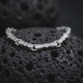 Load image into Gallery viewer, Polished silver Greek meander bracelet displayed across textured black volcanic rock, highlighting the sculpted geometric links and continuous recessed pattern in a premium macro studio photograph.
