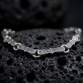 Load image into Gallery viewer, Oxidized sterling silver Greek key bracelet arranged on dark volcanic rock, showing elongated engraved meander links and circular connectors in a detailed macro studio close-up.
