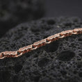 Load image into Gallery viewer, The rose gold plated meander bracelet is displayed across black volcanic rock, emphasizing its slim profile, sculpted bar links, and ancient Greek detailing in a refined macro image.
