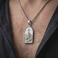 Load image into Gallery viewer, The polished silver Christian pendant is worn on a man’s chest, with Jesus beneath the cross, radiant background lines, and the arched medallion shape clearly visible in a premium lifestyle photograph.
