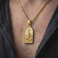 Load image into Gallery viewer, A gold plated INRI Jesus pendant is worn on a man’s neck with dark clothing, highlighting the dimensional cross-bearing scene and symbolic religious details in a refined close-up.
