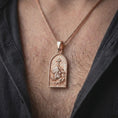 Load image into Gallery viewer, The rose gold plated Jesus carrying the cross pendant is worn on a man’s chest, showcasing the raised Christian imagery, sculpted garments, and devotional arched design in an elegant lifestyle shot.
