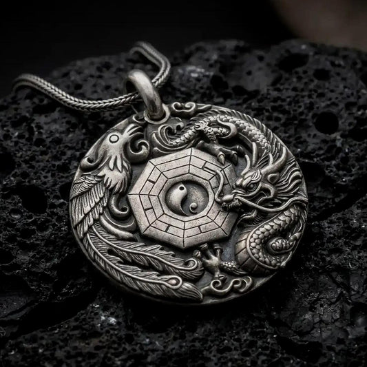 An oxidized dragon and phoenix pendant rests on dark volcanic rock, showing the central Yin Yang symbol, octagonal Bagua design, detailed scales, flowing feathers, and cloud motifs in a macro studio close-up.