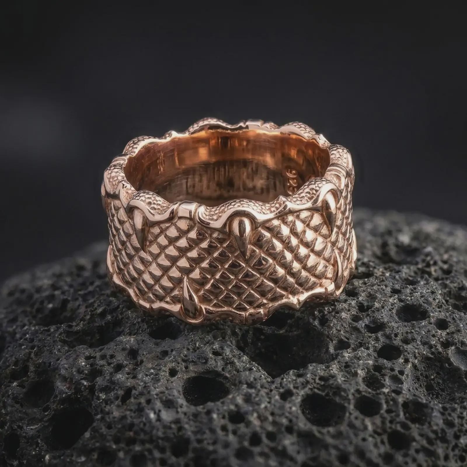 The rose gold plated fantasy claw ring is arranged on black volcanic rock, emphasizing its wide profile, layered scale texture, and mythical dragon-inspired construction in a refined macro image.