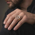 Load image into Gallery viewer, The rose gold plated Norse Viking ring is worn on a man’s finger, showcasing the interlocking triangle motif, skull detail, engraved runes, and rugged masculine proportions in an elegant lifestyle close-up.
