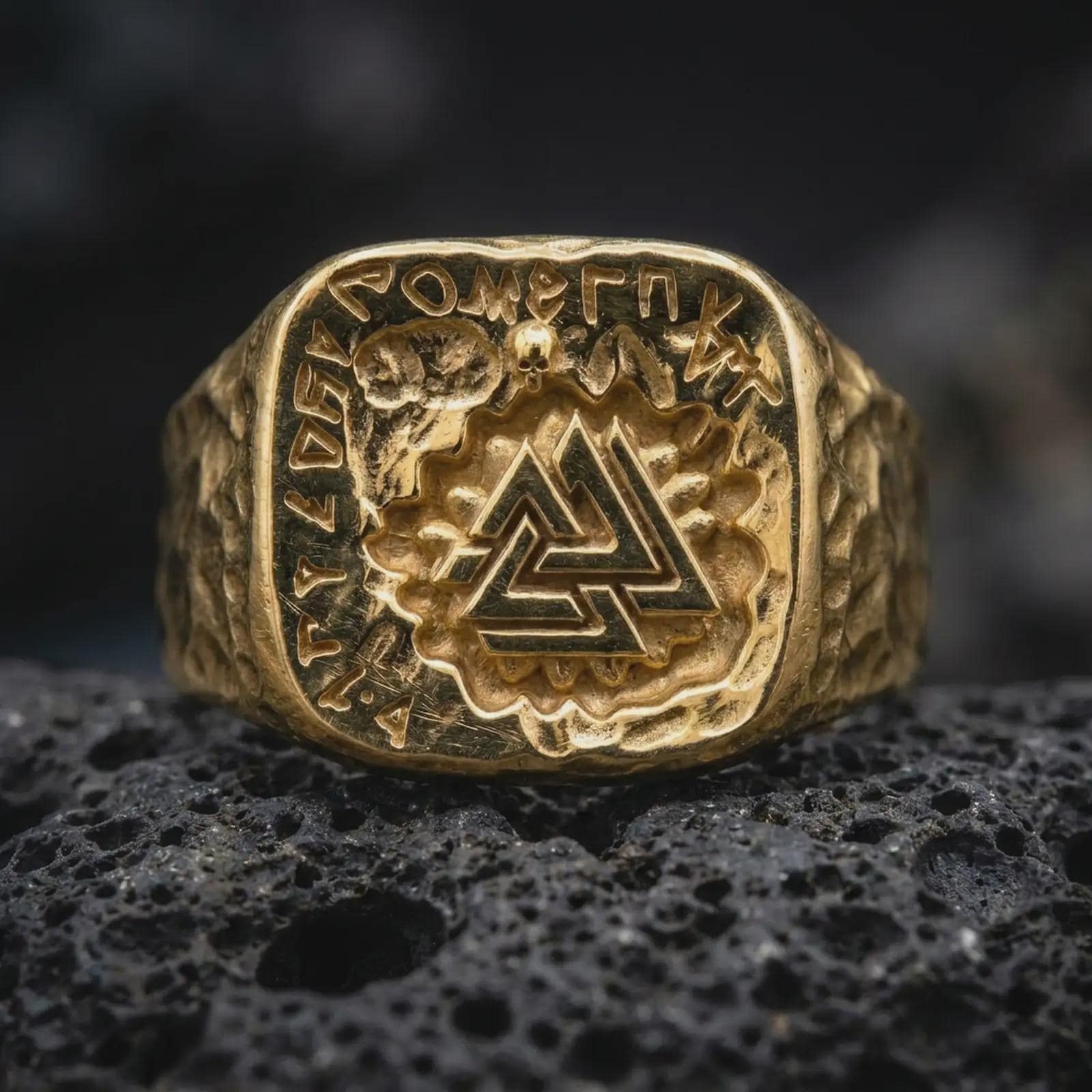 A gold plated Norse rune ring rests on rugged volcanic rock, featuring a raised Valknut symbol surrounded by ancient-style lettering and a small skull detail in a luxury macro studio close-up.