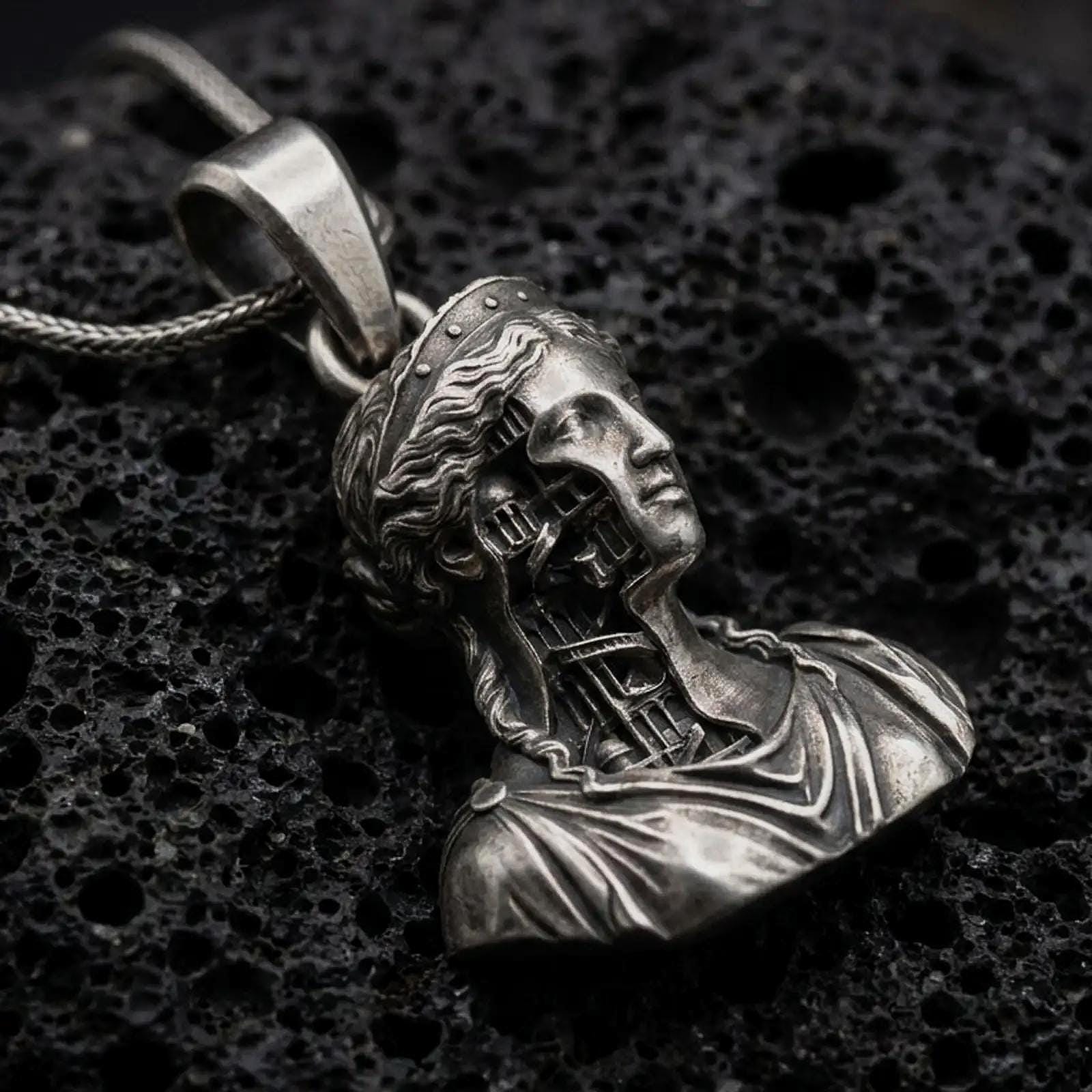Oxidized architectural bust pendant resting on volcanic rock in dark macro studio close-up