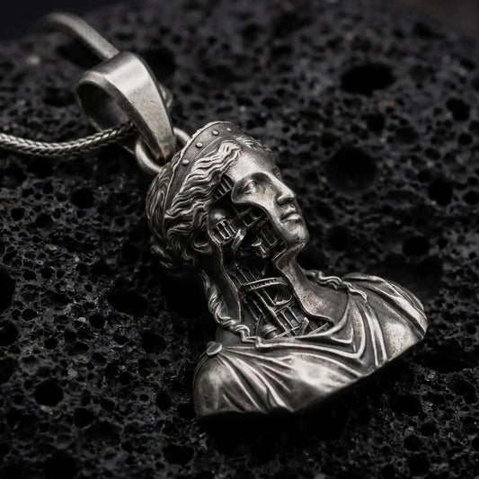 Oxidized architectural bust pendant resting on volcanic rock in dark macro studio close-up