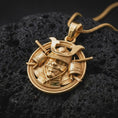 Load image into Gallery viewer, A gold plated Japanese samurai pendant lies on dark volcanic rock, featuring a fierce armored warrior, crossed weapon elements, and an ornamental circular frame in a luxury macro studio close-up.
