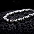 Load image into Gallery viewer, The polished silver Greek meander necklace is displayed across textured black volcanic rock, highlighting the repeating ancient Greek key pattern and articulated link construction in a detailed macro photograph.
