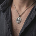 Load image into Gallery viewer, An oxidized octopus pendant is worn on a man’s neck, displaying the dark recessed texture, raised sea creature motif, and flowing tentacle details in a masculine lifestyle close-up.
