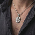 Load image into Gallery viewer, The polished silver octopus necklace is worn on a man’s chest, showing the round medallion shape, dimensional marine design, and detailed suction cups in a premium lifestyle photograph.
