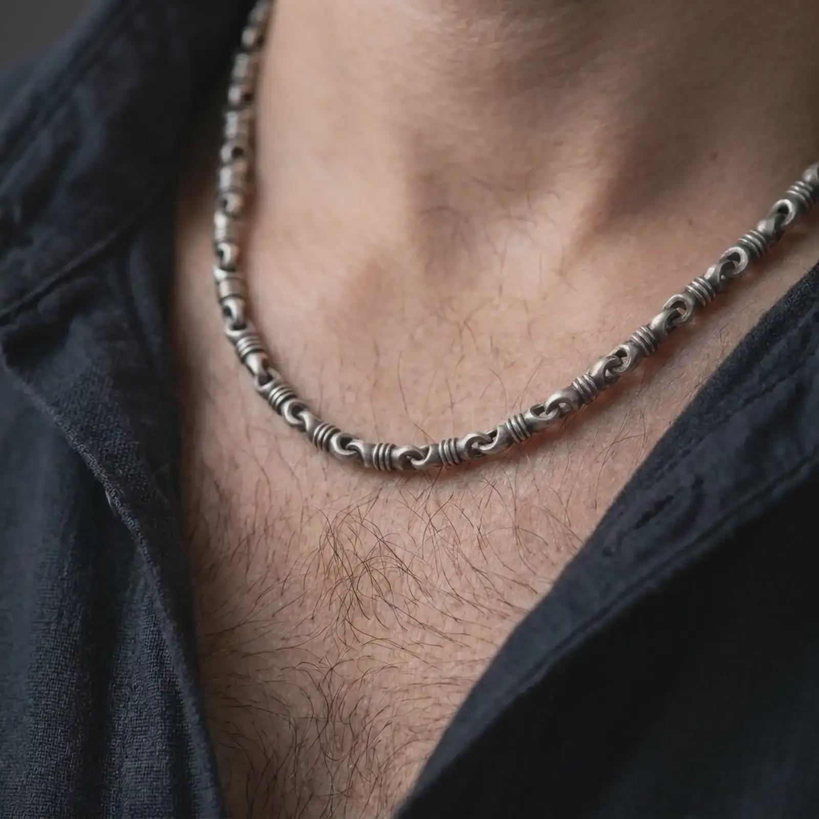 A ridged barrel chain necklace with an oxidized finish is worn on a man’s neck, displaying dark recessed details, rounded connectors, and a bold masculine silhouette in a close-up lifestyle shot.
