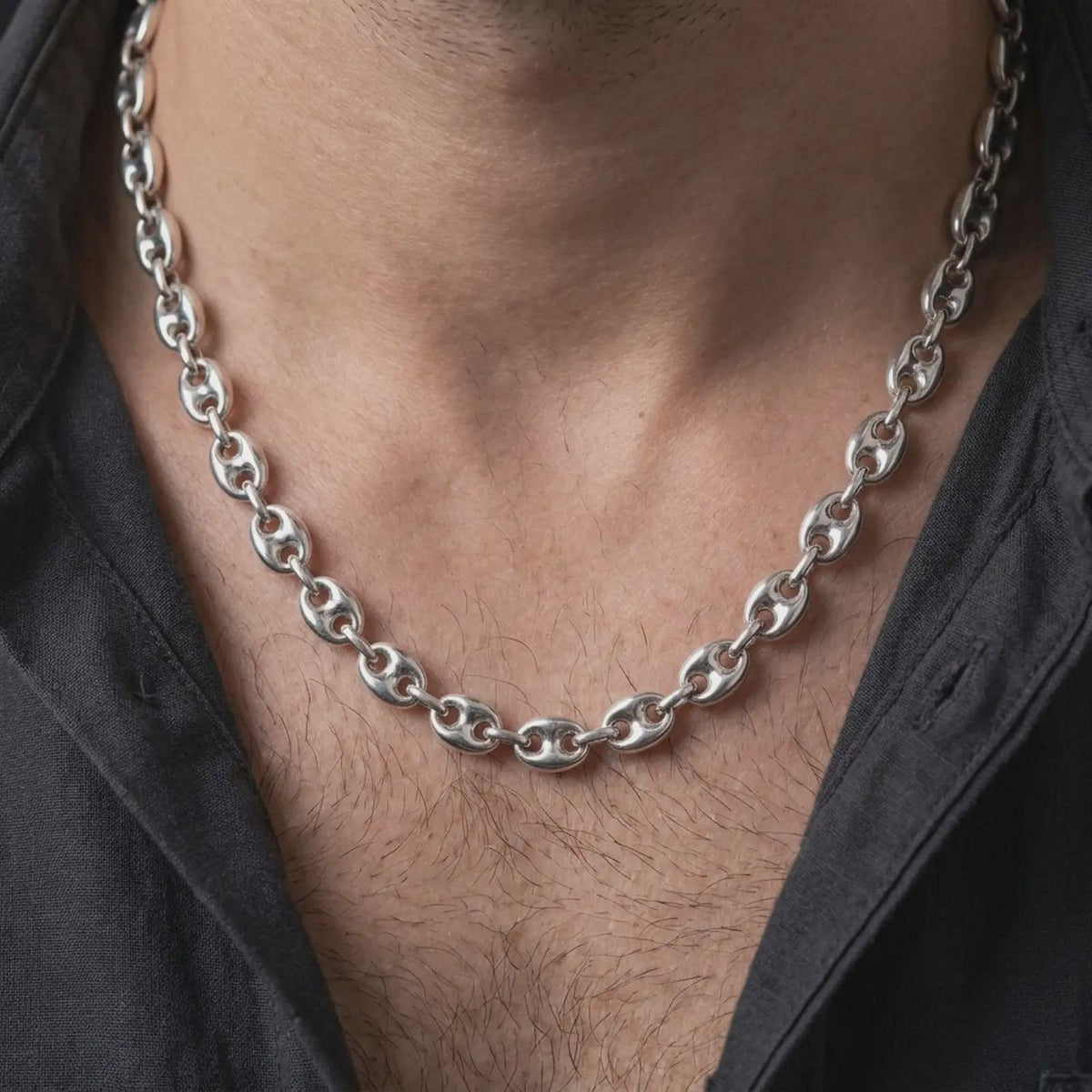 The polished silver 11mm mariner necklace is worn on a man’s chest, showing its substantial oval links and structured central-bar design in a detailed lifestyle photograph.