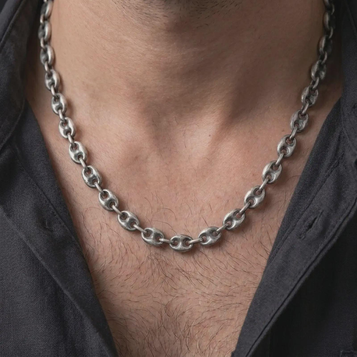 An 11mm mariner chain necklace with an oxidized finish is worn around a man’s neck, displaying the darkened recesses and bold anchor-inspired links in a masculine lifestyle close-up.
