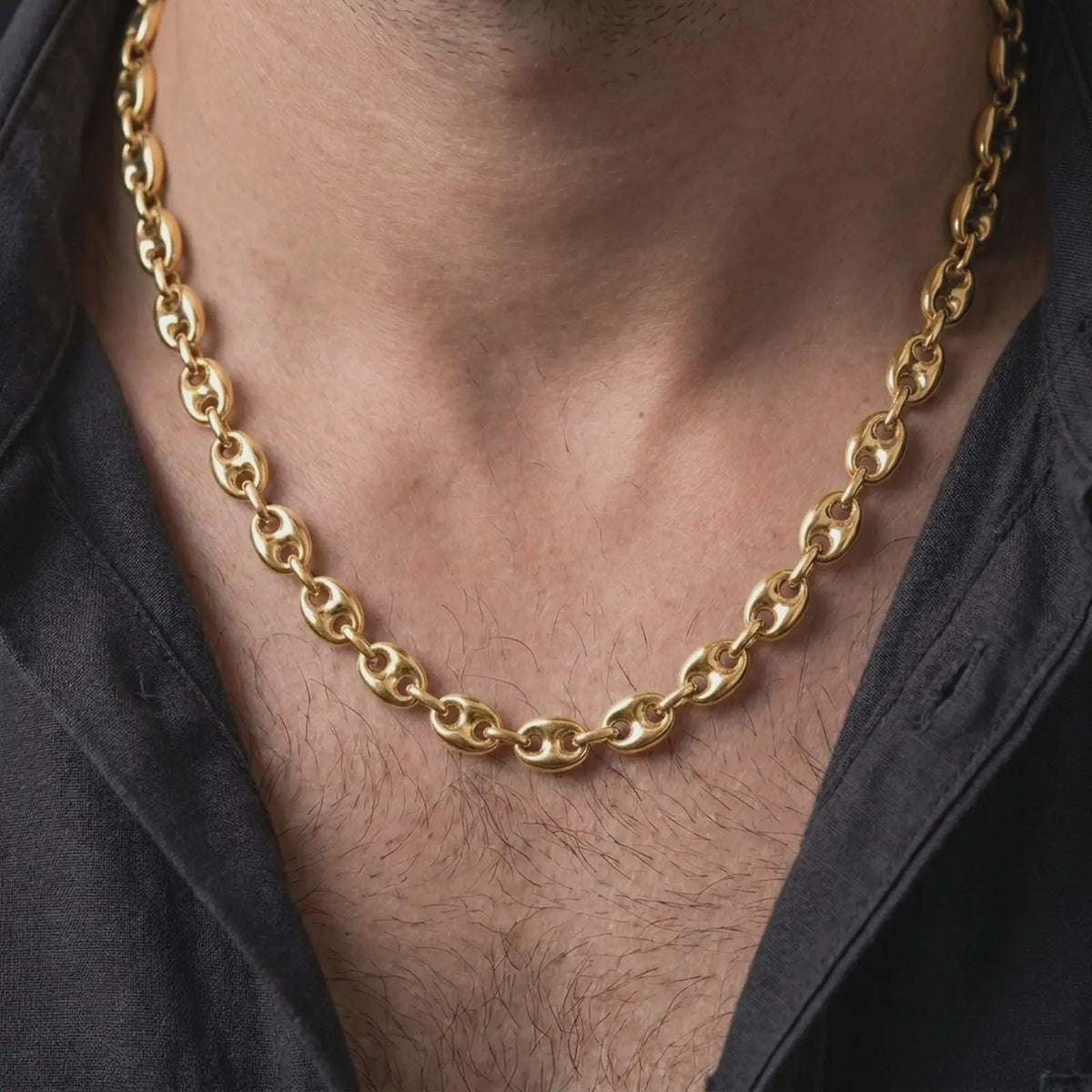 A gold plated 11mm anchor link chain is worn on a man’s neck with dark clothing, highlighting its wide maritime links and polished statement profile in a premium close-up.