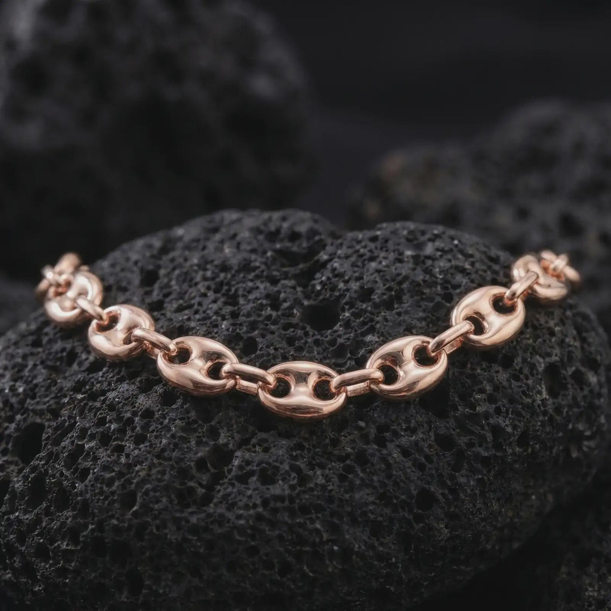 The rose gold plated 11mm mariner chain necklace rests on black volcanic rock, emphasizing its wide interlocking links and strong nautical profile in a refined macro studio image.