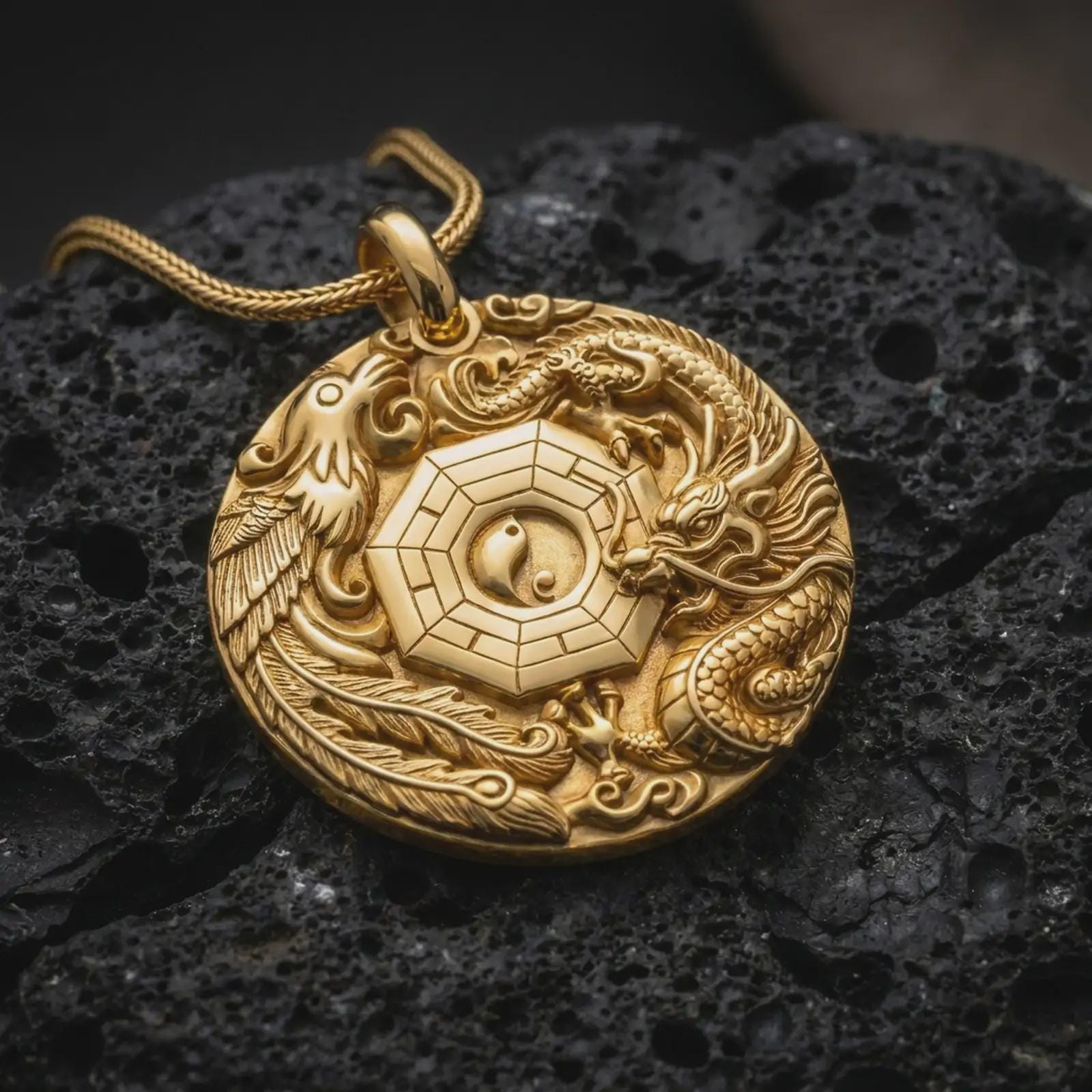 A gold plated Chinese dragon and phoenix pendant lies on rugged volcanic rock, featuring a central Yin Yang emblem, Bagua-inspired lines, layered scales, ornamental feathers, and symbolic cloud details in a luxury macro close-up.