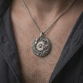 Load image into Gallery viewer, An oxidized dragon and phoenix pendant is worn on a man’s neck, displaying the dark recessed details, central Yin Yang symbol, Bagua geometry, and mythical creature relief in a masculine lifestyle close-up.
