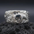 Load image into Gallery viewer, The polished silver dolphin band is displayed on textured black volcanic rock, highlighting the smooth marine figure, layered wave relief, and broad sculptural profile in a detailed macro photograph.
