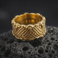 Load image into Gallery viewer, A gold plated dragon scale ring rests on rugged volcanic rock, featuring dimensional reptile scales and pointed claws wrapped around the upper and lower edges in a luxury macro studio close-up.
