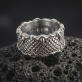 Load image into Gallery viewer, The polished silver dragon claw ring is displayed on textured black volcanic rock, highlighting the repeating scale pattern, sculpted talons, and substantial unisex band in a detailed macro photograph.
