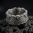 Load image into Gallery viewer, An oxidized sterling silver dragon scale ring rests on dark volcanic rock, showing deeply carved reptilian scales and raised claws gripping the wide band in a premium macro studio close-up.
