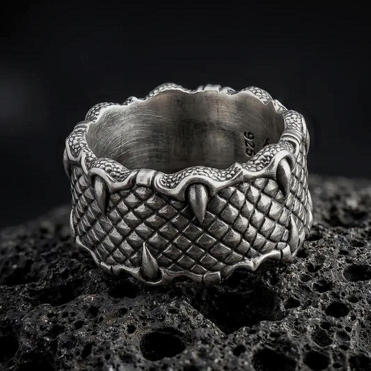 An oxidized sterling silver dragon scale ring rests on dark volcanic rock, showing deeply carved reptilian scales and raised claws gripping the wide band in a premium macro studio close-up.