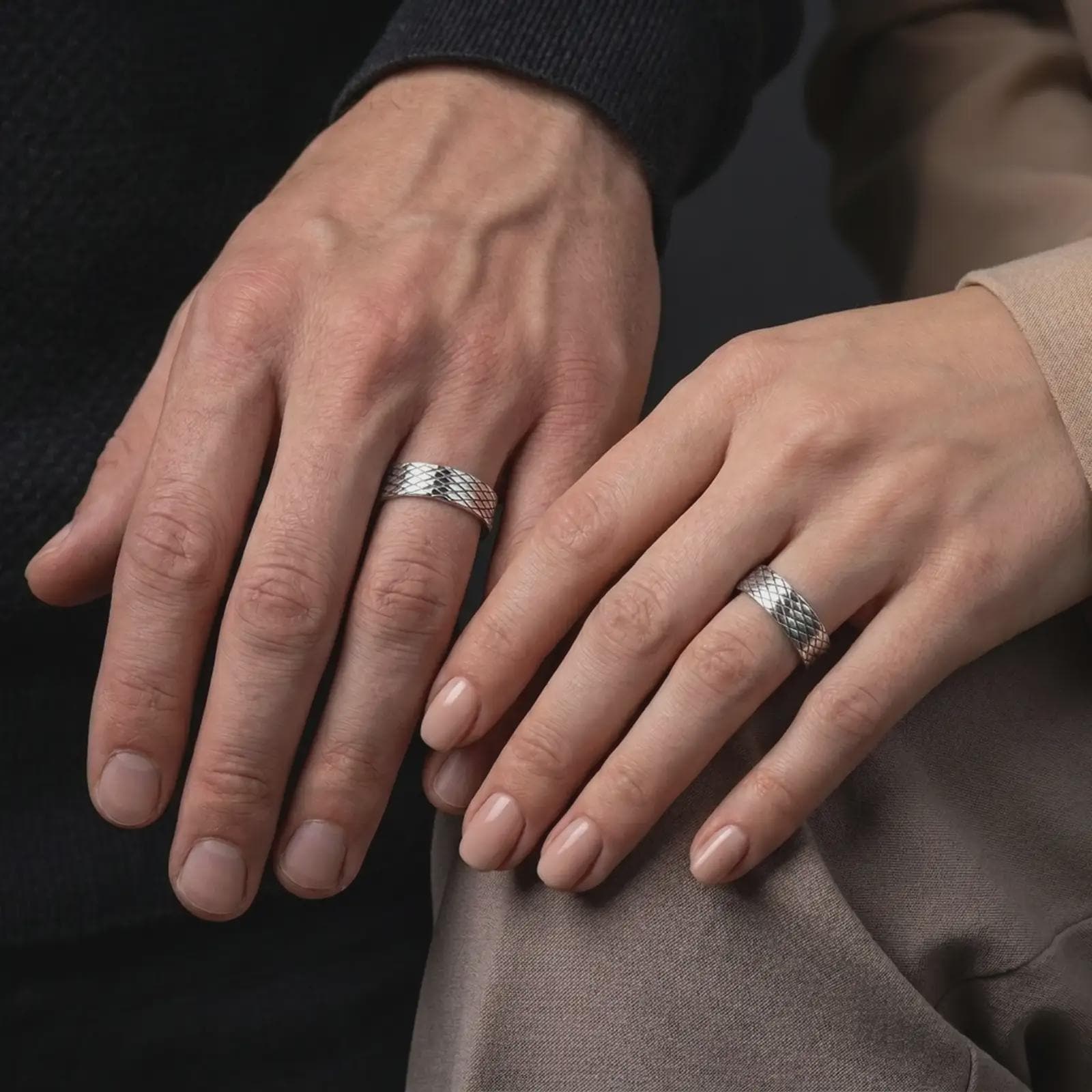 The polished silver crosshatch bands are worn by a couple, showing the continuous diamond pattern and balanced unisex proportions in a premium close-up lifestyle photograph.