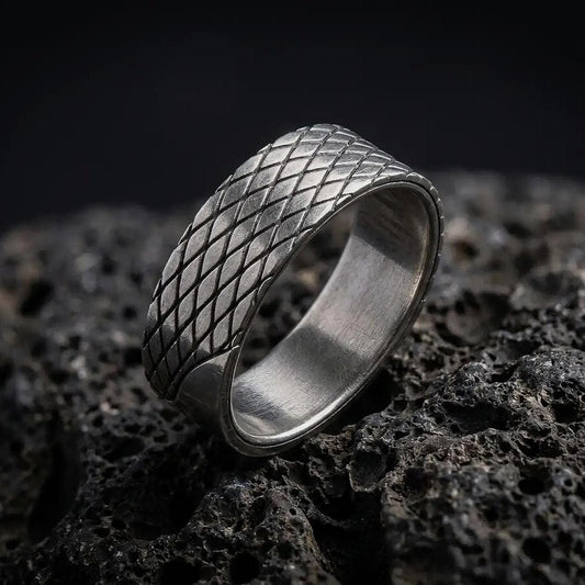 An oxidized sterling silver lattice ring stands on dark volcanic rock, showing its continuous diamond-shaped crosshatch pattern and recessed diagonal grooves in a premium macro studio close-up.