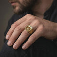 Load image into Gallery viewer, A gold plated Valknut signet ring is worn on a man’s finger, highlighting the raised geometric symbol, Norse rune detailing, and substantial warrior-inspired construction in a refined close-up lifestyle shot.
