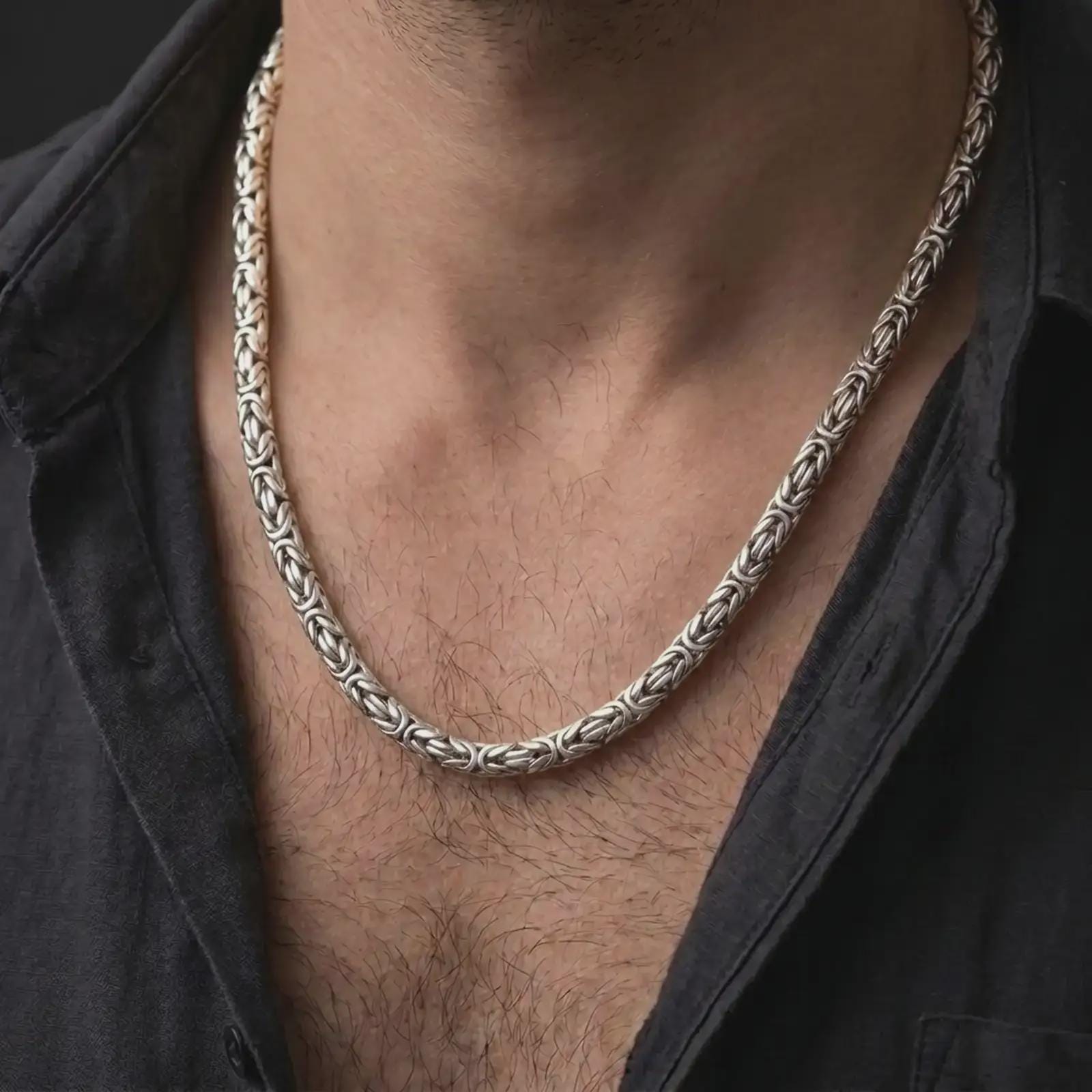 The polished silver Byzantine necklace is worn on a man’s chest, showing the rounded interlocking links and substantial 6mm chain width in a premium lifestyle photograph.