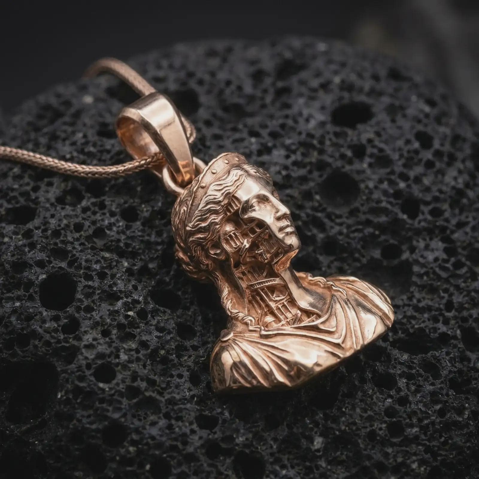 Rose gold plated architectural bust pendant on volcanic rock in dark macro studio close-up