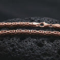 Load image into Gallery viewer, The rose gold plated 4mm square Byzantine chain necklace is arranged on black volcanic rock, featuring a detailed square link structure and elegant woven pattern in a high-end macro image.
