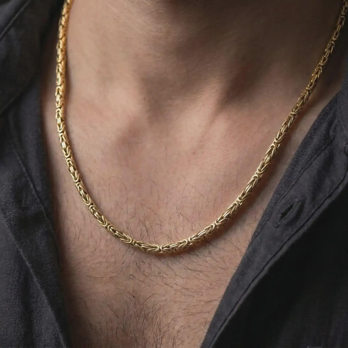 A gold plated 4mm round Byzantine chain necklace is worn on a man’s neck with dark clothing, highlighting the woven link texture and balanced statement profile in a refined close-up.