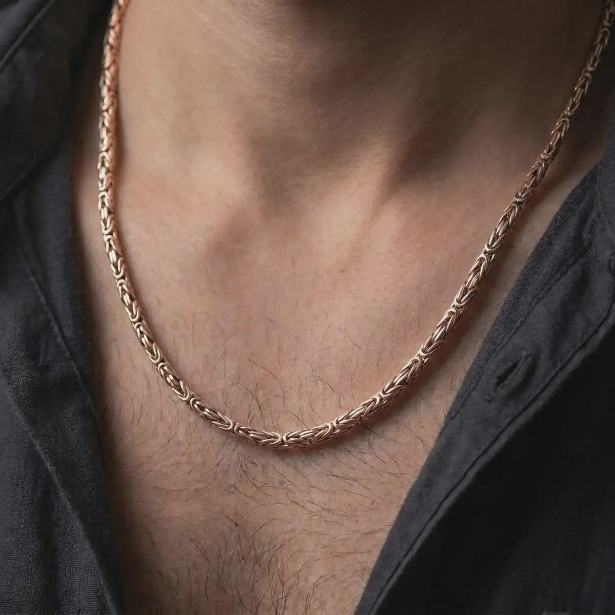 The rose gold plated Byzantine necklace is worn naturally on a man’s chest, showcasing its round interwoven chain structure, dimensional shine, and elegant masculine design.