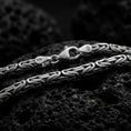 Load image into Gallery viewer, A 4mm round Byzantine chain necklace with an oxidized finish rests on dark volcanic rock, showing its compact interwoven links and dimensional sterling silver texture in a macro studio close-up.
