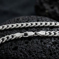 Load image into Gallery viewer, The polished silver 5mm Cuban chain necklace is displayed across textured black volcanic rock, highlighting the interlocking curb link pattern and secure clasp in a premium macro photograph.
