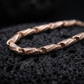 Load image into Gallery viewer, The rose gold plated meander link necklace is arranged on black volcanic rock, emphasizing its geometric Greek key engravings, smooth connectors, and refined chain structure in a macro studio image.
