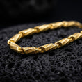 Load image into Gallery viewer, A gold plated Greek key chain necklace lies on rugged volcanic rock, featuring rectangular engraved links with continuous meander details in a luxury macro studio close-up.
