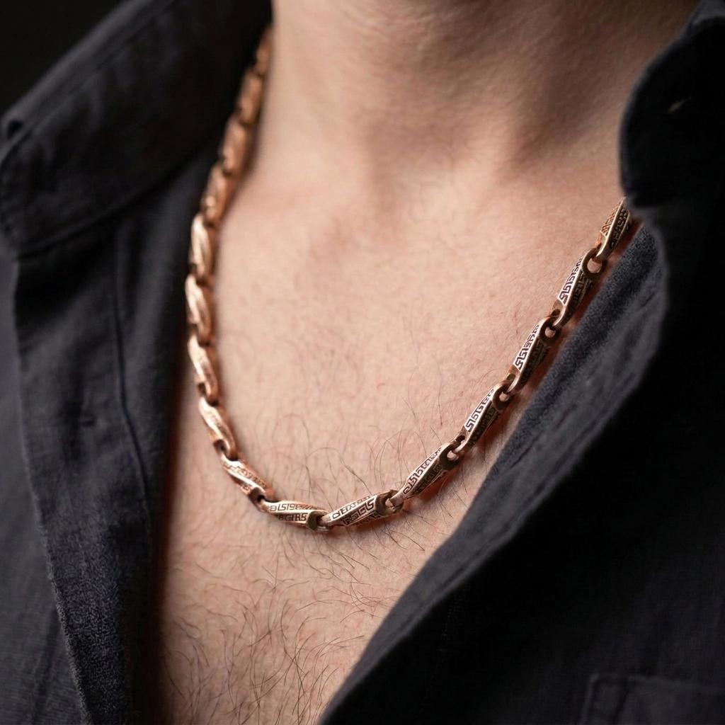 The rose gold plated Greek meander necklace is worn naturally on a man’s chest, showcasing the engraved geometric links and symbolic ancient Greek design in an elegant lifestyle close-up.