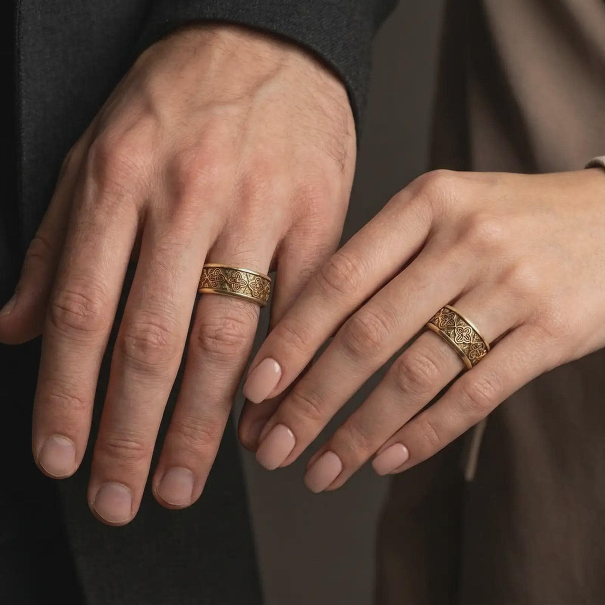 A gold plated floral wedding band is worn on a finger, highlighting the ornamental flower pattern and meaningful alternative wedding ring style in a refined close-up lifestyle shot.