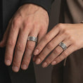 Load image into Gallery viewer, The polished silver flower spinner band is worn on a finger, showing the repeating floral relief and smooth everyday ring profile in a premium lifestyle photograph.
